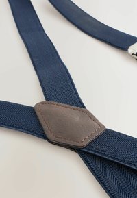 Tengerészkék felfüggesztők halszálkás mintával, barna bőr folttal és kontrasztos varrással. A végén látható a fém beszerelés.