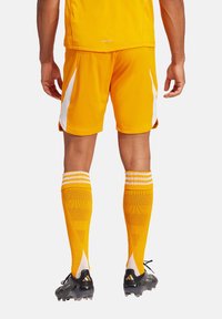 Gele sporttrui en korte broek met witte accenten, gecombineerd met gele kniehoge sokken met een textuurdesign en zwarte voetbalschoenen.