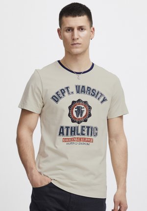Beige T-Shirt mit Rundhalsausschnitt, marineblauem Kragen. Das Frontgraphic zeigt fetten Text "Dept. Varsity Athletic" mit einem Schild und orangefarbigen Akzenten.