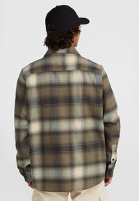 Checkered flannel shirt featuring shades of brown, cream, and black. Loose fit, buttoned cuffs, and a collared neck. Textured fabric.