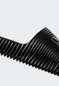 Sort fleksibel bølgeplastslange med accordion-lignende folder, bøjet mod en ensfarvet lys grå baggrund.