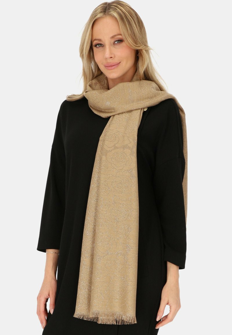 Beżowy szalik z kwiecistym wzorem i subtelnym połyskiem, z frędzlami na końcach. Nosi się luźno na czarnym topie. Miękka tekstura.