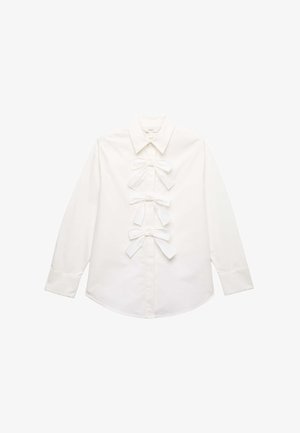 Hvid skjorte med lange ærmer, spids krave og tre dekorative stofsløjfer ned langs midten foran.