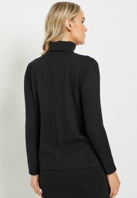 Haut à col roulé noir en tissu doux, avec des manches longues, un col haut et un design à dos lisse et sans couture.