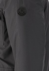 Svart jackärm med slät tygtextur. Har ett runt svart logopatch med bergsdesign och texten "WHISTLER".