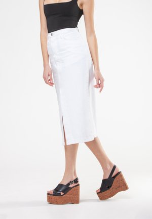 Gonna midi in denim bianco con uno spacco frontale, abbinata a sandali con zeppa neri con piattaforma in sughero e dettaglio con fibbia in parte.