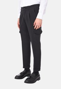 Pantaloni neri sartoriali con fronte plissettato e vita elastica, dotati di tasche cargo sui lati e orli risvoltati. Abbinati a scarpe nere.