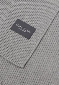 Γκρι ριβέ ύφασμα κασκόλ με μια μαύρη ετικέτα μάρκας "Marc O'Polo EST. IN STOCKHOLM" να διακρίνεται prominently στην γωνία.