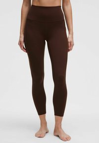Pruunid kõrge taljeega legginsid, mis on valmistatud elastsetest materjalidest, omavad siledat tekstuuri ja sobivat disaini, mis kitseneb pahkluude juures.