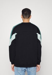Sudadera negra con acentos diagonales en turquesa y azul claro en los hombros. Presenta un cuello redondo y puños acanalados, fabricada con una tela suave.