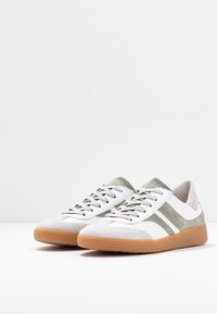 Pair of white and light gray sneakers with green stripes and gum rubber soles, angled slightly to the right on a white surface.