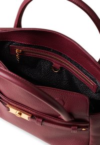 Burgunderfarbene Lederhandtasche mit strukturiertem Äußeren, ausgestattet mit einem Innenfach mit goldfarbenem Reißverschluss und einem schwarz gemusterten Futter.