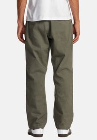 Olive green cotton pants with a relaxed fit, featuring straight legs and a smooth texture. Worn with a white shirt and sneakers.