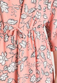 Ljusrosa blommig klänning med svarta bladmönster, med en rynkad midja med snörning och silverfärgade detaljer. Trekvartsärmar.