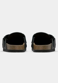 Sorte lærsandaler med korksåle, åpen bak, og to justerbare stropper med spenner. Teksturert såler for godt grep og holdbarhet.