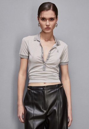 Polo grigio aderente con scollo a V, maniche corte e colletto a contrasto. Abbinato a pantaloni in pelle nera a vita alta.