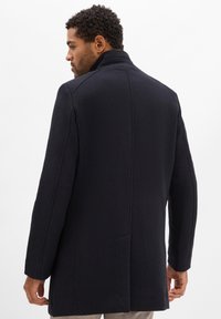 Schwarzer Wollmischungs-Mantel mit strukturiertem Design, hohem Kragen und taillierter Passform. Auffällige Nähte und eine glatte, leicht strukturierte Oberfläche.