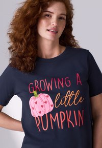 Tumesinine puuvillane t-särk, millel on graafiline kujundus roosa kõrvitsa ja värvilise kirjaga teksti "Growing a little Pumpkin" (Kasvatan väikest kõrvitsat).