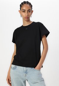 Black short-sleeved t-shirt made of cotton, featuring a round neckline and a small logo detail on the chest, worn with light blue jeans.