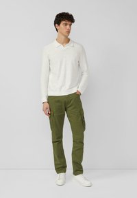 Hellgraues Polohemd mit langen Ärmeln und Kragen, kombiniert mit olivgrünen Cargo-Hosen mit seitlichen Taschen. Das Model trägt weiße Turnschuhe.