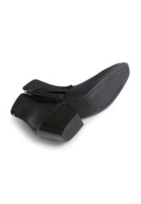 Botín negro de cuero hasta el tobillo con un tacón bajo y cuadrado, cremallera frontal y borlas decorativas; textura suave y diseño de punta afilada.