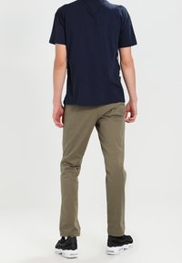 T-shirt blu navy a maniche corte abbinata a pantaloni slim-fit verde oliva. Sneakers nere con suola bianca. Sfondo neutro.