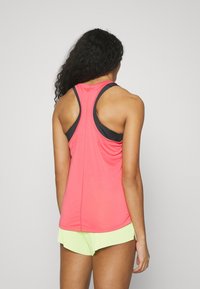 Różowy sportowy top na ramiączkach z designem racerback, z czarnymi akcentami i lekką, gładką teksturą, w połączeniu z jasnobeżowymi szortami.