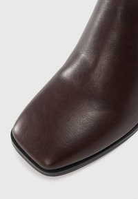 Dunkelbraune Lederstiefel mit quadrater Zehenform und glatter Textur, vor einem schlichten hellen Hintergrund gezeigt.