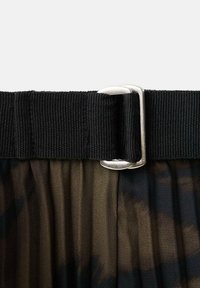 Cintura in tessuto nero con fibbia metallica argento, sopra un tessuto trasparente plissettato in colori scuri, caratterizzato da motivi e trame sottili.