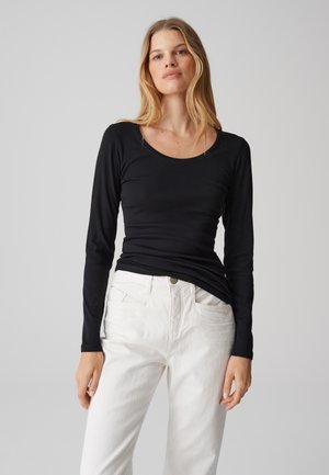 Maglietta nera a maniche lunghe con scollatura a barca, realizzata in tessuto morbido; abbinata a pantaloni bianchi a vita alta con tasche e chiusura a bottone.