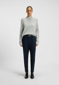 Ljusgrå, texturerad stickad tröja med hög hals, matchad med marinblå högmidjade byxor och glänsande svarta ankboots.