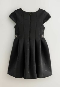 Schwarzes Kleid mit kurzen Ärmeln, das ein strukturiertes Muster aus Schleifen und Buchstaben aufweist. Reißverschluss hinten und ein ausgestellter Rock. Goldene Akzentdetails.