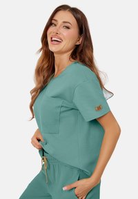 Szmaragdowy top z krótkim rękawem, z teksturowaną kieszonką, okrągłym dekoltem oraz metką na rękawie; w zestawie z dopasowanymi teksturowanymi spodniami.