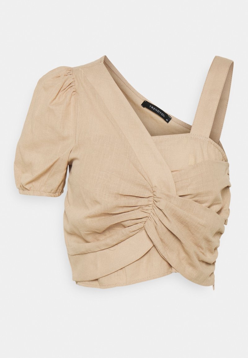 Haut court beige froncé à enroulement avec une manche courte bouffante d'un côté et une large bretelle de l'autre, fabriqué en tissu léger texturé.