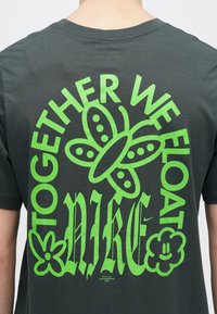 T-shirt cinza escuro com um grande design gráfico verde com o texto "JUNTOS FLOTA-MOS" e ícones de borboleta, planta e rosto sorridente.