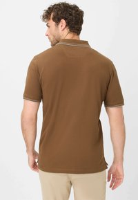 Polo marrone con maniche corte, caratterizzato da un colletto classico e dettagli a righe in contrasto sui polsini. Texture morbida e liscia.