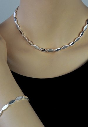 Silberne Halskette und Armband mit ovalen Gliedern in einer Mischung aus polierten und strukturierten Oberflächen auf dunklem Hintergrund.