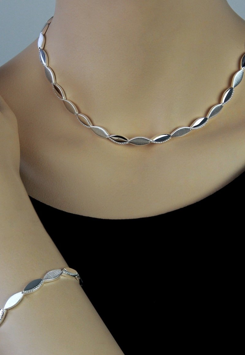 Collier et bracelet en argent avec des maillons ovales présentant un mélange de finitions polies et texturées sur un fond sombre.