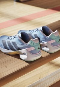 Paar blaue Sportschuhe mit weißen Sohlen, die auf hölzernen Turnhallen-Bänken im natürlichen Licht ruhen.