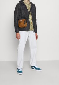 Giacca trapuntata nera, maglione a maglia multicolore, pantaloni bianchi, sneakers blu e una borsa a tracolla marrone con dettagli a patta e cerniera.