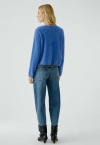 Himmelblauer, kuscheliger Pullover mit kastigem Schnitt, kombiniert mit hoch taillierten Jeans aus Denim. Die Jeans verfügen über zwei Gesäßtaschen und einen lockeren Schnitt.
