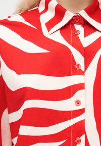 Gros plan sur une chemise boutonnée rouge et blanche avec des rayures abstraites semblables à celles d'un zèbre et un col pointu.