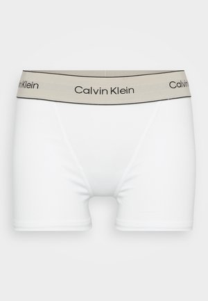 Bijele pamučne bokserice s bež elastičnom gumicom s logotipom "Calvin Klein", crnim obrubom i glatkom, rastezljivom teksturom.