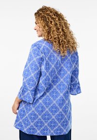 Blauw gebloemd topje met een geometrisch ontwerp, driekwart mouwen en gerimpelde zoom. Lichtgewicht stof met een ontspannen pasvorm.