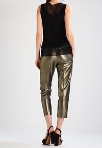 Top negro sin mangas con una espalda transparente, combinado con pantalones cortos metálicos dorados, que cuentan con un acabado texturizado y sandalias de tacón negro.