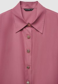 Blusa color rosato con colletto classico e bottoni decorativi di varie texture, realizzata in tessuto leggero.