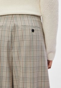 Calças às riscas em bege, com tecido texturizado, detalhe de botão preto e bolsos traseiros, com um corte tailored e perna larga.