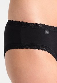 Black cotton brief with lace trim along the waistband, featuring a soft texture and a logo tag on the side. Mid-rise cut.