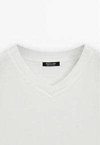 Witte V-halstrui van zacht materiaal; heeft een geribde textuur bij de kraag. Etiket geeft aan dat het merk Massimo Dutti is, vervaardigd in Portugal.