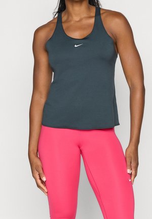 Athletische Person trägt ein dunkelgraues Nike Tanktop und auffällig pinke Nike Leggings, steht vor einem schlichten hellen Hintergrund.